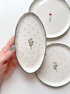 three plates with flowers painted on them are being held by a woman's hand