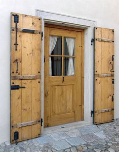 two wooden doors are open in front of a white building with stone floors and cobblestone flooring