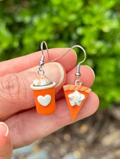 a hand holding two small earrings with orange and white designs on it's sides