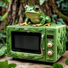 a frog sitting on top of a green microwave oven in front of some plants and trees