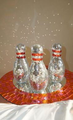 three shiny glass bowling pins sitting on top of a red tray with disco balls around it