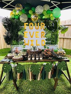 a table topped with lots of food under a tent covered in green and yellow balloons