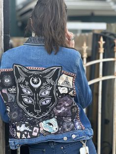 "Black Cat Reworked Jean Jacket" is an upcycled denim jacket embellished with vibrant fabrics, Black Cat patch, fabric print, and ribbon. These patterns are cut and pieced in abstract and traditional shapes, creating a "head turning", one-of-a-kind fashion statement. Your jacket is sure to be the talk of the evening or the concert! The jacket has been washed and is in excellent condition.  This jacket is an Old Navy brand, Women's sized M.  Handwash only for upkeep and to preserve appearance.  All sales are final. Please reach out to us for additional information or photos. Ready to ship Approximate Measurements: Sleeves: 24" Shoulder: 18" Length: 20" Punk Jean Jacket, Weird Clothing, Reworked Jeans, Apparel Design Inspiration, Upcycled Denim Jacket, Patch Jacket, Cat Patch