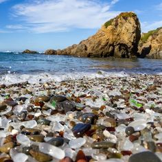 the beach is covered with many different colored rocks and glass pebbles, as well as waves coming in from the ocean