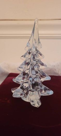 a clear glass christmas tree sitting on top of a red velvet covered tablecloth with white trim