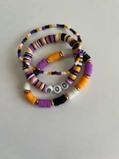 three bracelets with beads and letters are on a white surface, one is purple, the other is yellow