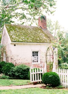 an old brick house with a white picket fence in front of it and a green roof