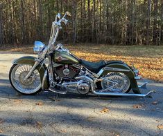 a green motorcycle parked on the side of a road in front of some trees and grass