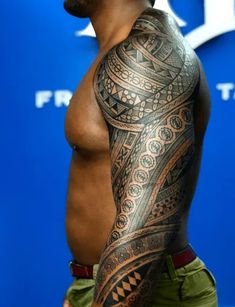 a man with a tattoo on his arm and chest standing in front of a blue wall