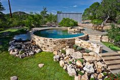 an aerial view of a pool surrounded by rocks and grass with stairs leading up to it