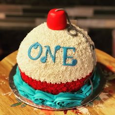 a cake that has the word one on it with blue and red frosting, sitting on top of a wooden table