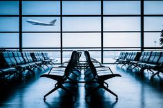 an airport terminal filled with lots of empty chairs and planes flying in the sky behind them