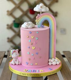 a pink cake decorated with rainbows and clouds