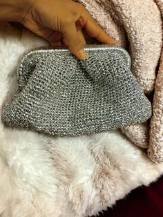 a woman's hand holding onto a silver purse on top of a fluffy white blanket