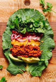 a hamburger with lettuce, onions and sauce on it sitting on top of a wooden cutting board