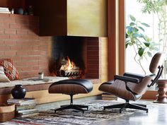 an eames chair and ottoman in front of a fireplace