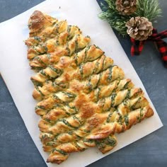 a pastry shaped like a christmas tree on top of a cutting board next to pine cones