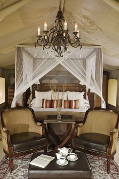 a bedroom with a canopy bed, two chairs and a coffee table in front of it