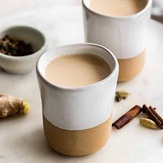 two white cups filled with liquid next to cinnamons