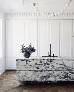 an elegant kitchen with marble counter tops and white cabinets, along with a vase filled with purple flowers