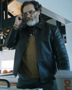 a man in a leather jacket talking on a cell phone while standing next to a counter