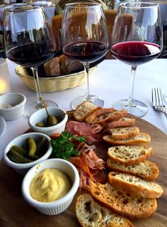 a wooden board topped with lots of food next to wine glasses