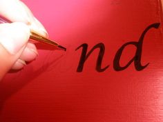 a person writing on a red piece of paper with a pen in their left hand