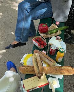 people sitting at a picnic table with bread, tomatoes, cheese and other food items