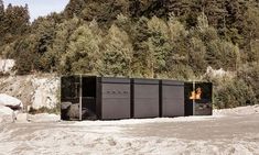 three black boxes sitting on top of a dirt field next to trees and rocks in front of a mountain