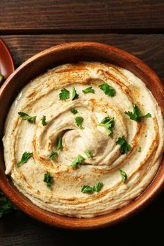 a wooden bowl filled with hummus and garnished with cilantro leaves