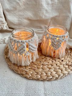 two mason jars with candles in them sitting on a wicker basket next to a white blanket