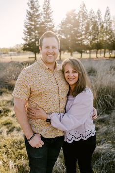 a man and woman are standing together in the grass with trees in the back ground