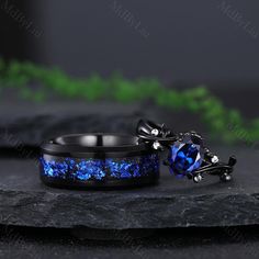 two rings with blue stones on them sitting on top of a black stone slab next to each other