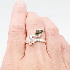 a woman's hand holding a ring with a green stone in it and two leaves on the band