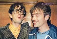 two young men standing next to each other in front of a door with their eyes closed