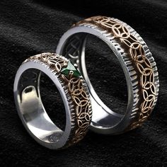 two wedding rings with gold and green accents on black fabric background, close up view