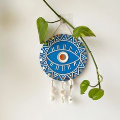 a blue and white clock with an evil eye hanging from it's side next to a plant