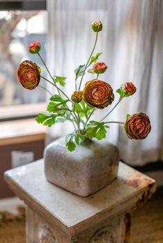 a vase filled with flowers sitting on top of a stone block in front of a window