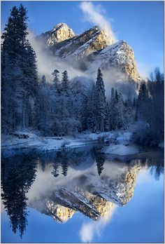 the mountains are covered in snow and trees, with water reflecting them on the surface