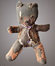 an old teddy bear is hanging upside down on a gray background with other items around it