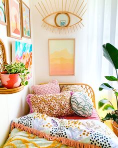 a bed with lots of pillows on top of it next to potted plants and pictures