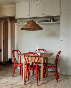 a dining room table with red chairs and a basket hanging from the ceiling over it