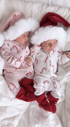 two baby babies wearing santa hats on top of a white sheet covered bed with red and white sheets