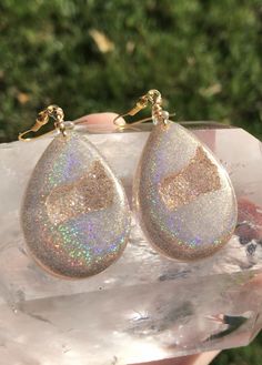 These holographic Teardrop geode earrings made from resin shift from clear gold to a beautiful sparkly rainbow. They are lightweight and won't bother your ears. Please be aware that resin is heat resistant up to 135 degrees. Wearing these earrings in extremely hot temperatures will cause them to be pliable. If this happens, simply place in a cooler location. I am not responsible for any damaged earrings due to extreme heat. Made by Katie Glover Resin Art by Katie 2020 Contact me on my Instagram Sparkling Dangle Teardrop Earrings Gift, Sparkling Teardrop Dangle Earrings As Gift, Hypoallergenic Resin Jewelry For Parties, Teardrop Sparkling Jewelry For Gift, Iridescent Sparkling Jewelry As Gift, Iridescent Sparkling Jewelry Gift, Sparkling Iridescent Jewelry As Gift, Sparkling Iridescent Jewelry For Gifts, Unique Gold Teardrop Earrings Gift