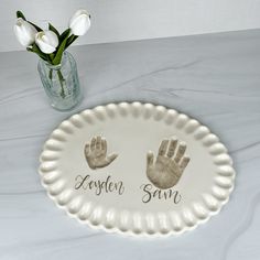 a white plate with two hand prints on it next to a vase filled with flowers