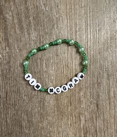 a green beaded bracelet with the word mom written on it and two white beads