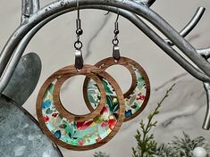 two wooden earrings hanging from a tree branch with flowers on it and one has a flowered circle in the center