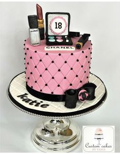 a pink cake with black and white designs on it's side, topped with cosmetics