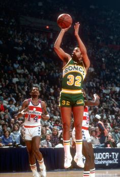 a basketball player jumping up to dunk the ball in front of two other players