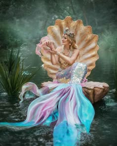 a mermaid sitting on top of a rock in the water with her hands up to her chest